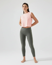 Woman wearing a watermelon pink airlite cropped active tank and gray leggings on a gray background