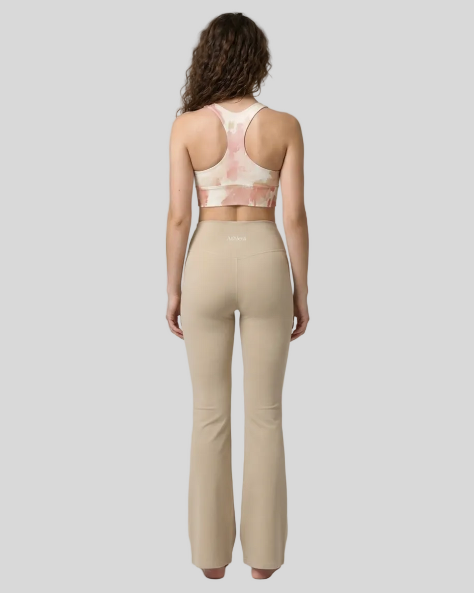 Back view of woman wearing a Blush Form Sports Bra in blush form print and yoga pant in warm sand on a plain background