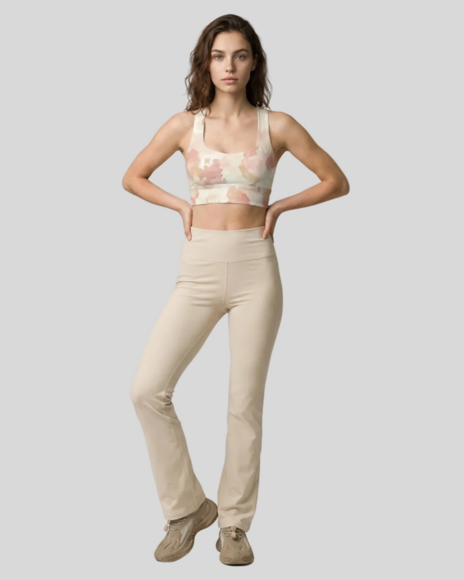 Woman wearing a Athlesi Blush Form sports bra in blush form print and yoga pants in warm sand on a light gray background
