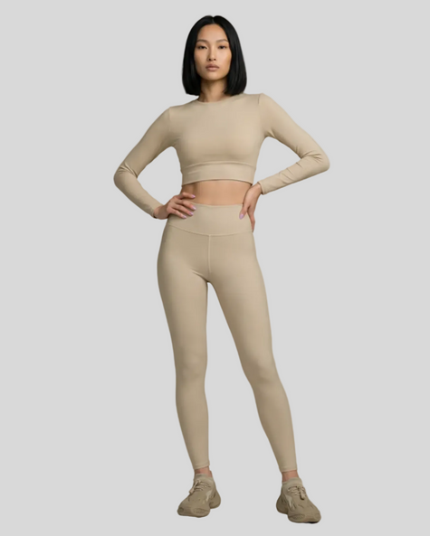 Front view of woman wearing warm sand Athlesi Blush Form long-sleeve cropped top and leggings on a light gray background