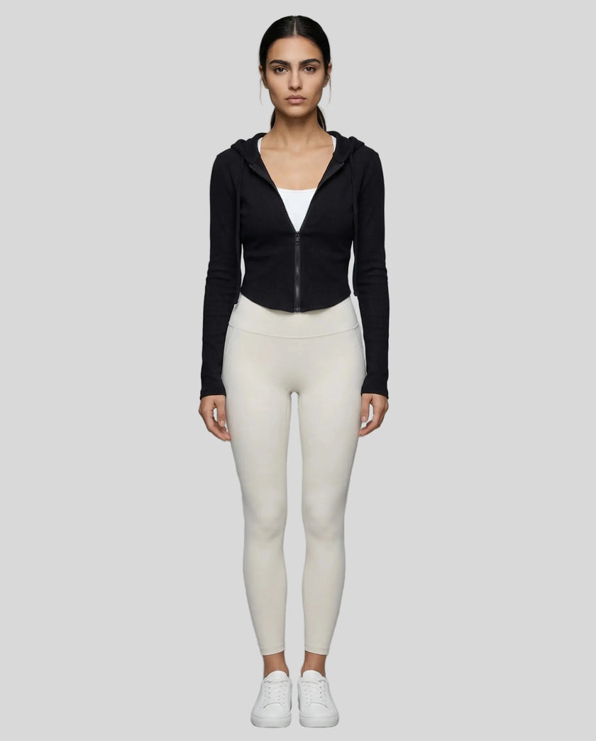 Model wearing a black ContourZip Ribbed Jacket and white leggings in a clean studio setting