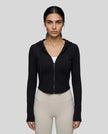 Mid shot of model wearing a black ContourZip Ribbed Jacket and white leggings in a clean studio setting