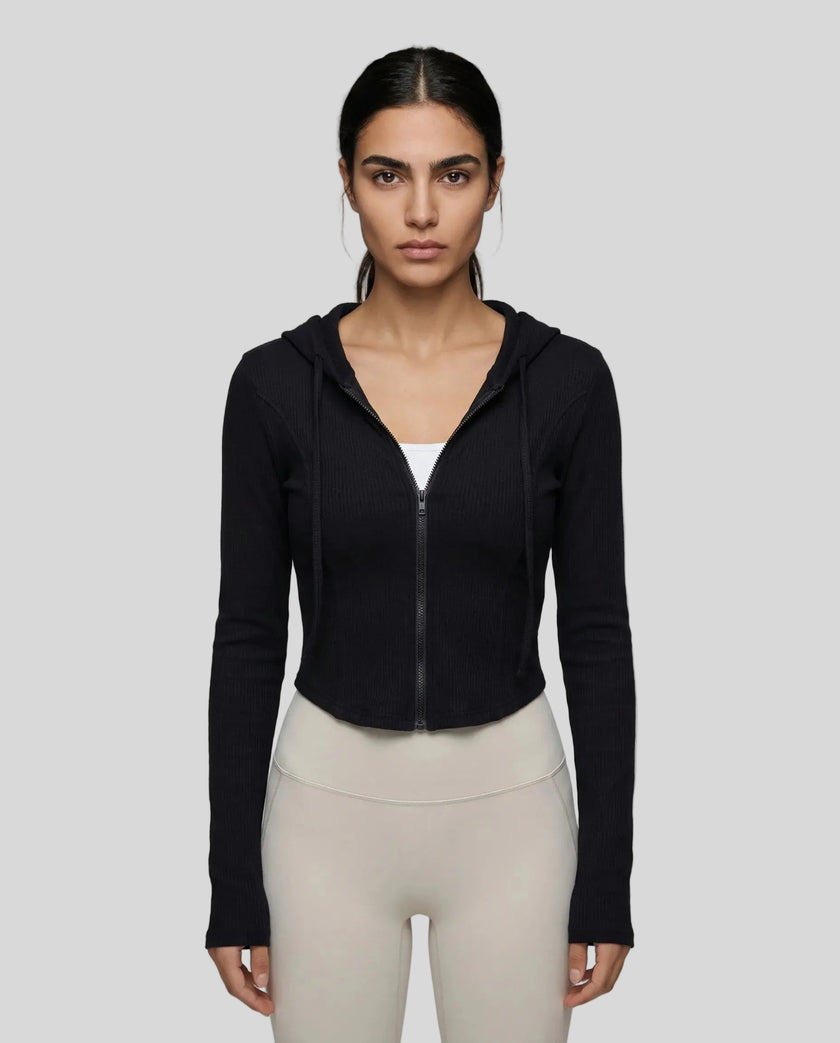 Mid shot of model wearing a black ContourZip Ribbed Jacket and white leggings in a clean studio setting