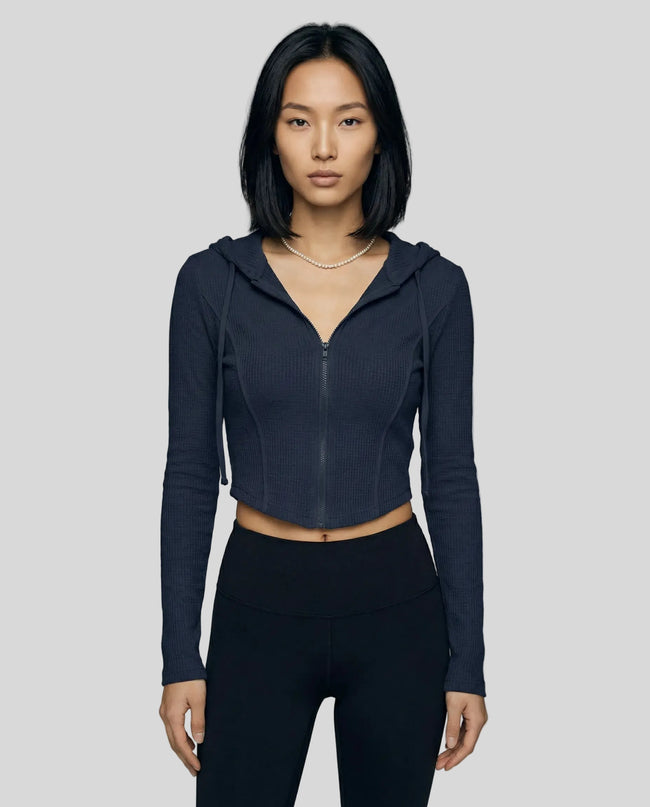 Mid shot of model wearing a navy blue ContourZip Ribbed Jacket and black leggings in a clean studio setting