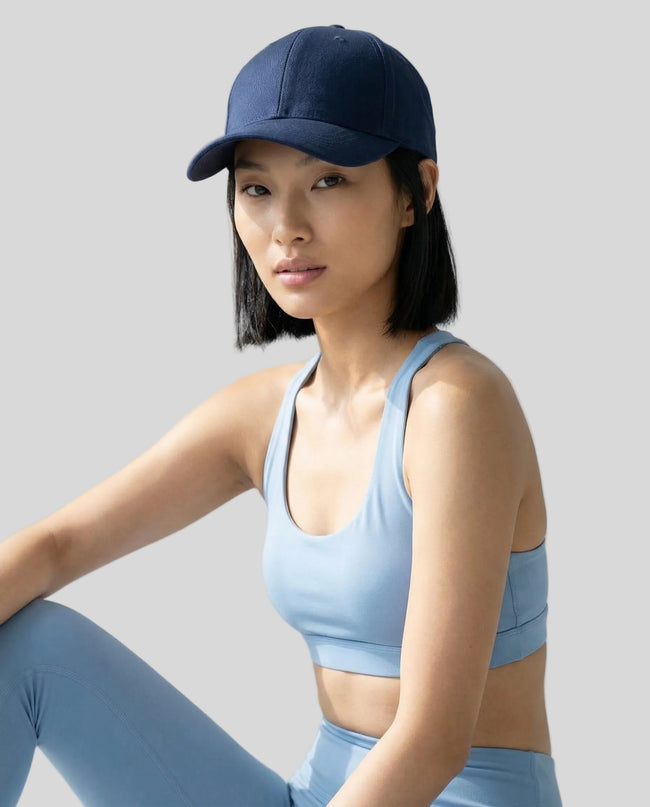 CoreForm Essential Cap in dark blue worn by model in a clean studio setting with a light blue sports bra and leggings