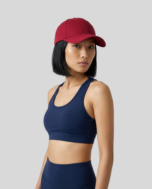 CoreForm Essential Cap in red worn by model in a clean studio setting with a navy sports bra and leggings