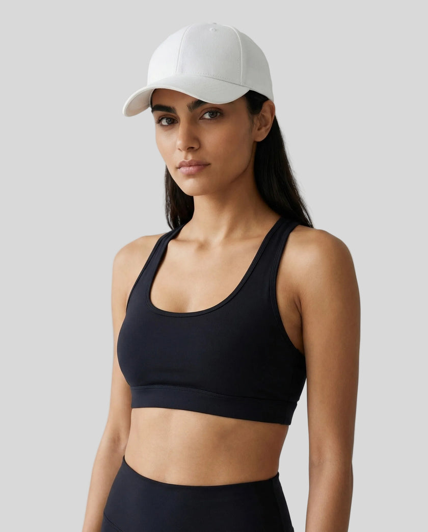 CoreForm Essential Cap in white worn by model in a clean studio setting with a black sports bra and leggings