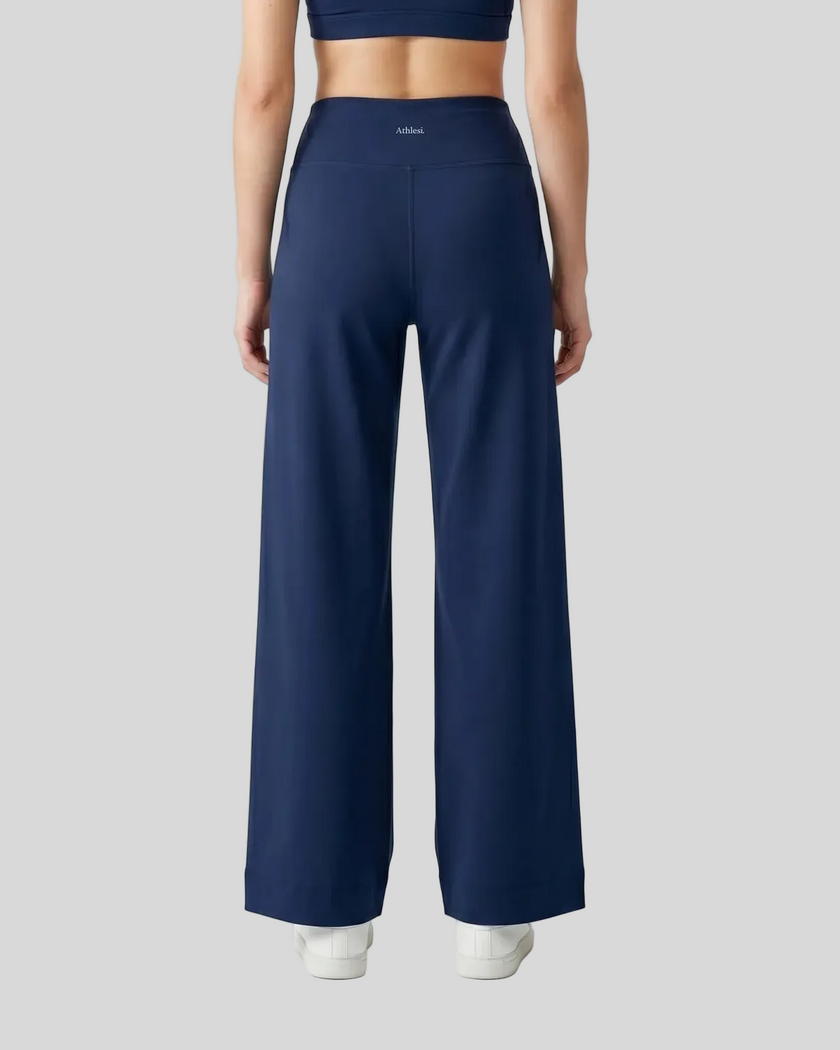 A model shown from the back wearing navy blue CoreLine Yoga Pants with a small white Athlesi logo on the waistband, paired with white sneakers against a clean white studio background.