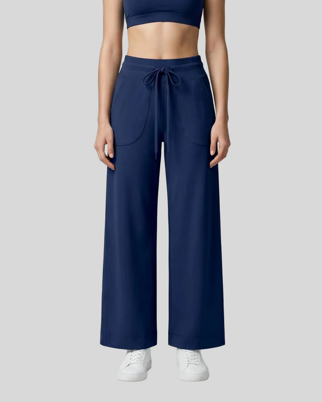 A model wearing navy blue CoreLine Yoga Pants with side pockets, paired with a matching navy crop top and white sneakers