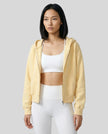 Model wearing a yellow CoreZip Hooded Jacket over a white sports bra and leggings on a neutral setting.