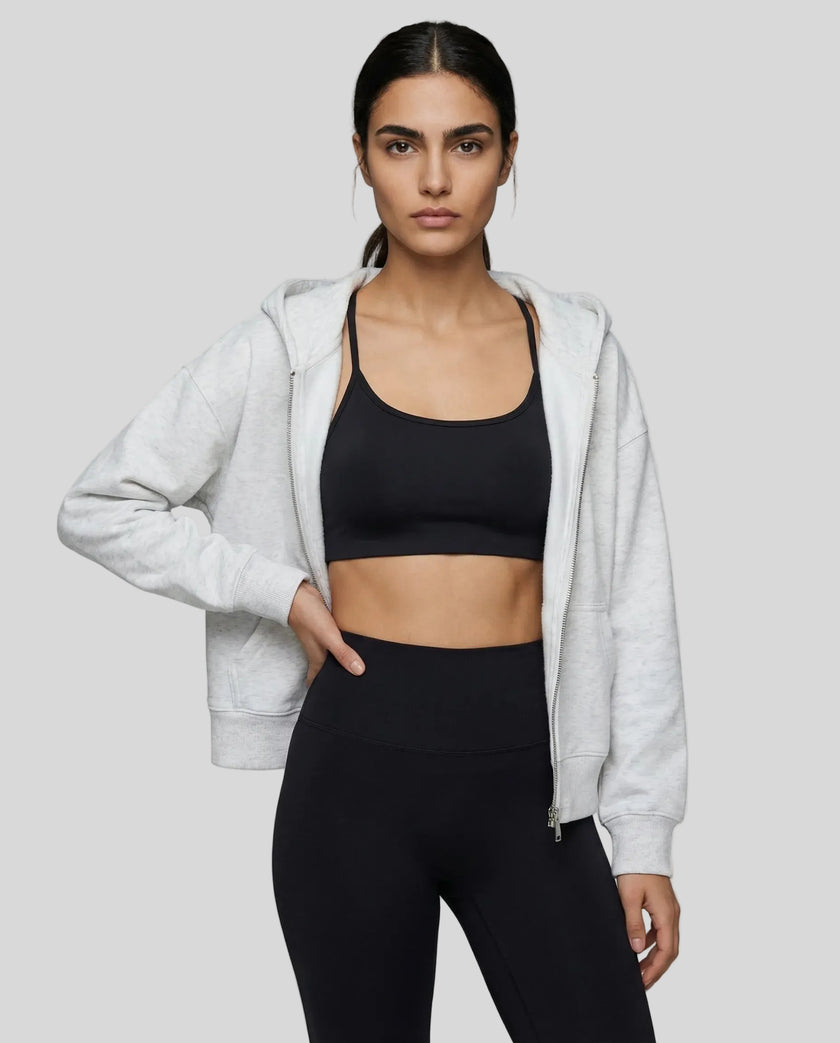 Model wearing a light gray CoreZip Hooded Jacket over a black sports bra and leggings on a neutral setting.