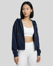 Model wearing a navy CoreZip Hooded Jacket over a white sports bra and leggings on a neutral setting.