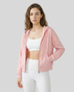 Model wearing a pink CoreZip Hooded Jacket over a white sports bra and leggings on a neutral setting.