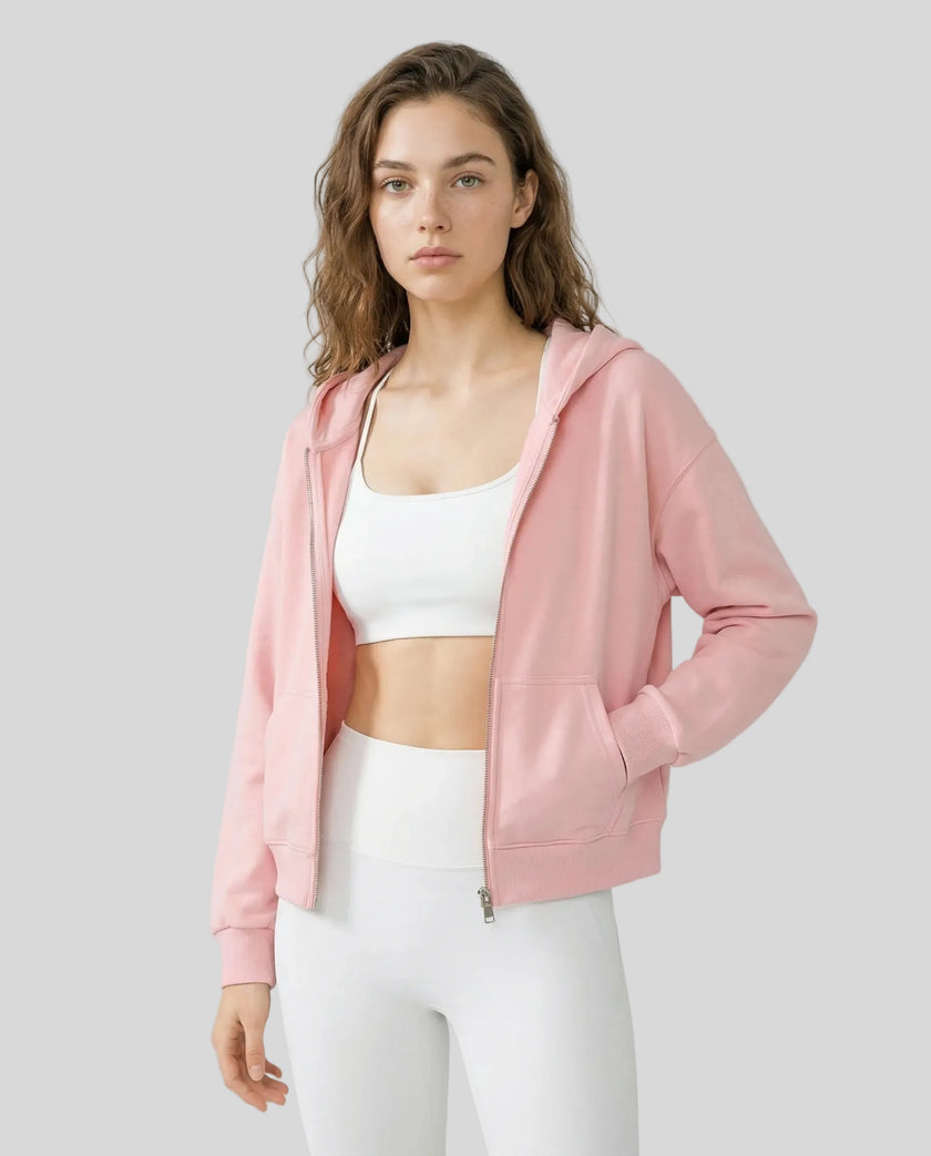 Model wearing a pink CoreZip Hooded Jacket over a white sports bra and leggings on a neutral setting.