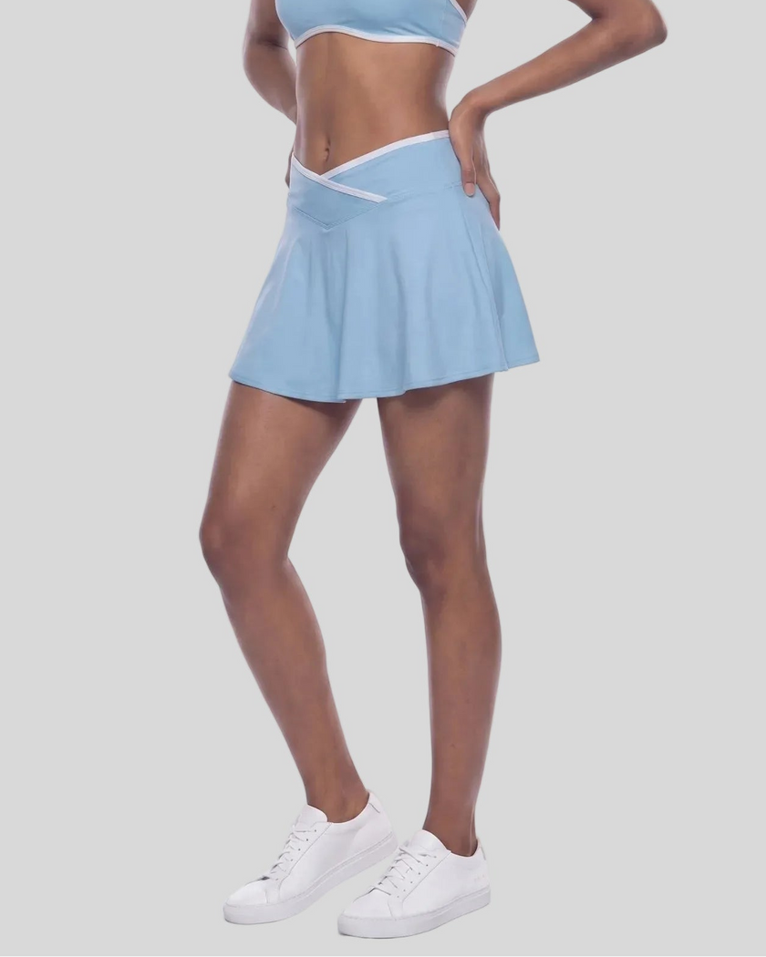 Lower body view of a model wearing a Sky Blue CourtClub Color Block A-Line Skirt, paired with a matching sky blue CourtClub Color Block Sports Bra and white sneakers.
