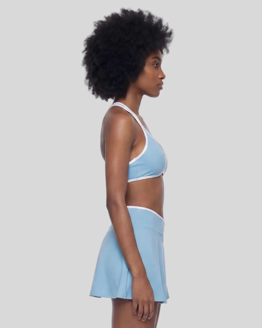 Side view of a model wearing the CourtClub Color Block Halter Sports Bra in Sky Blue