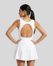 Woman wearing Athlesi CourtClub Open-Back Tennis Dress in White mid-body back view highlighting statement open-back detail