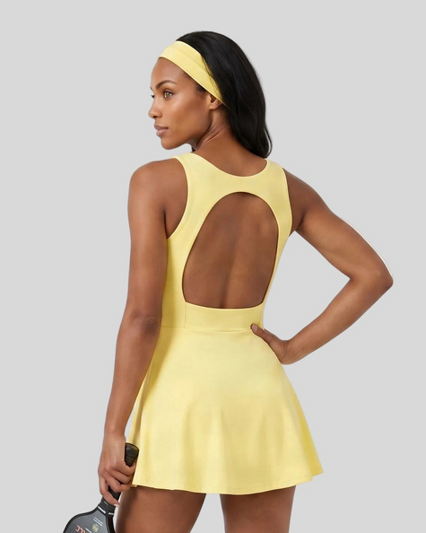 Woman wearing Athlesi CourtClub Open-Back Tennis Dress in Yellow mid-body back view highlighting statement open-back detail