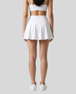 Back view of a model wearing the CourtClub Pleated Skirt in White