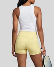 Woman wearing Athlesi CourtClub Tennis Short in Yellow mid-body back view highlighting sculpted waistband seam and fit