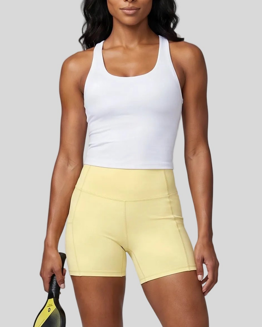 Woman wearing Athlesi CourtClub Tennis Short in Yellow mid-body front view highlighting waistband and fitted silhouette