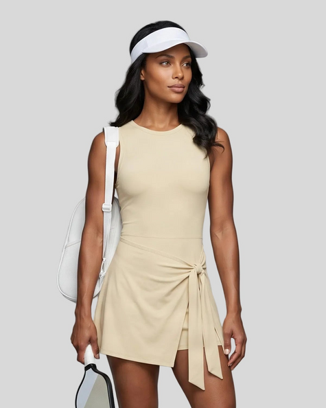 Woman wearing the Athlesi CourtClub Tie-Front Dress in Light Apricot, mid-body front view highlighting the asymmetric tie detail.