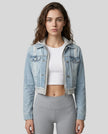 Woman wearing a light blue and gray Athlesi EdgeForm denim hoodie jacket with gray leggings, mid body front view on model showing cropped fit and layered hoodie 
