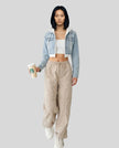 Front full body view of model wearing Athlesi EdgeForm light blue denim jacket over a white crop top and beige pants