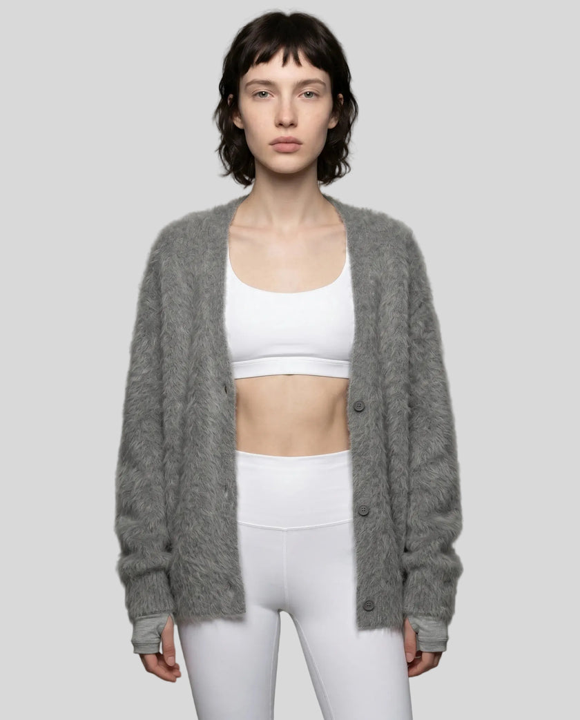 Woman wearing a dark gray cardigan over a white sports bra and leggings on a plain background