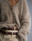 Person wearing a fluffy khaki cardigan and beige pants with a belt, on a plain background