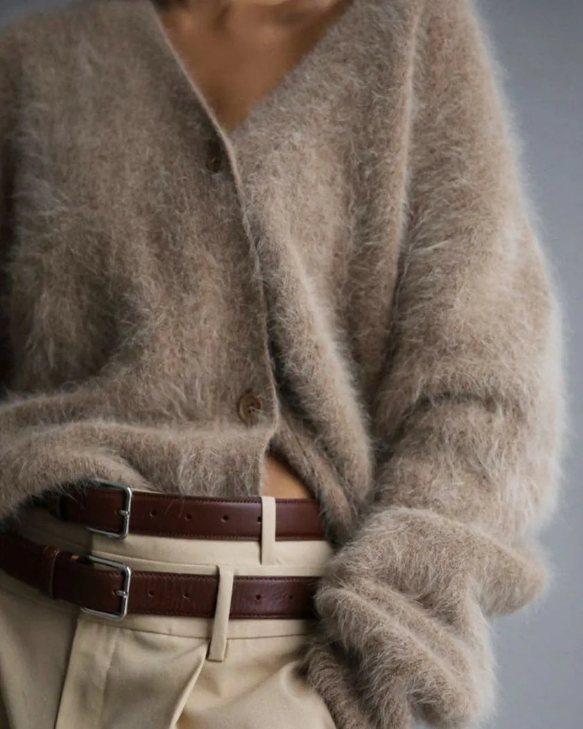 Person wearing a fluffy khaki cardigan and beige pants with a belt, on a plain background