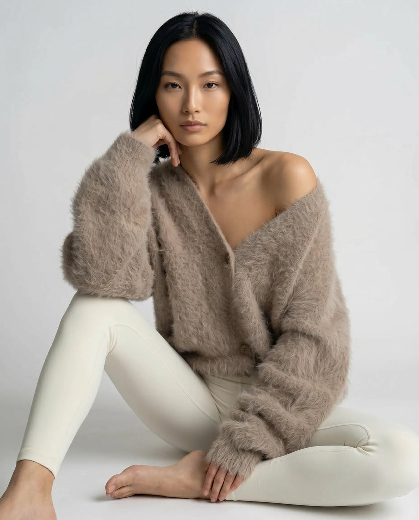 Woman wearing a khaki cardigan and white pants sitting on a white background