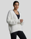Woman wearing a white fluffy cardigan over a black top on a gray background