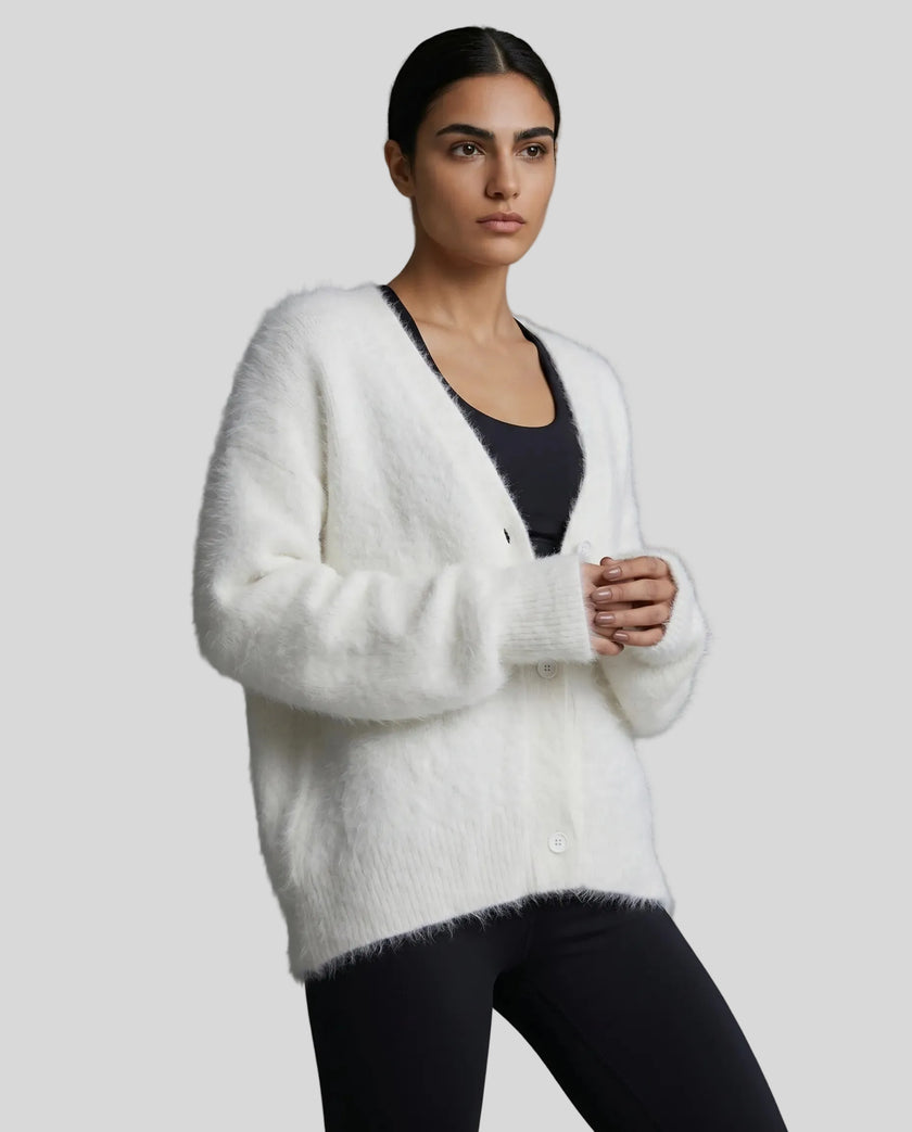 Woman wearing a white fluffy cardigan over a black top on a gray background