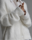 White fluffy cardigan worn over a white shirt on a gray background