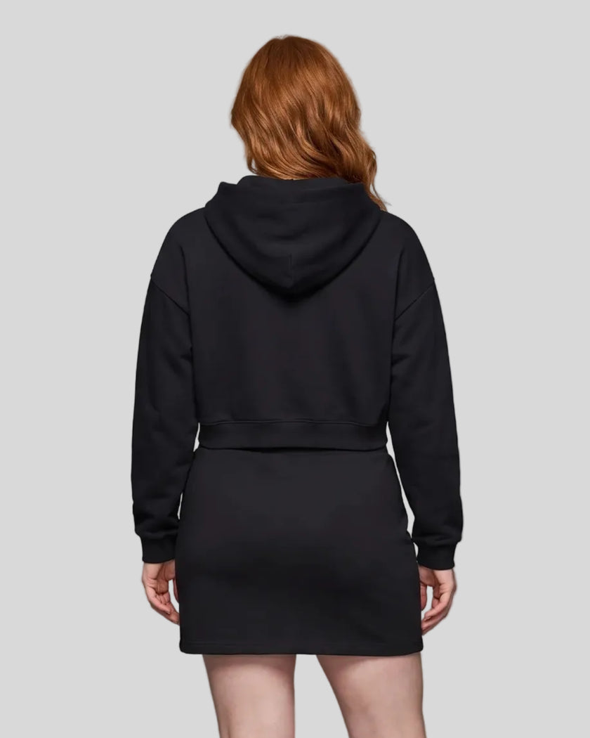 A model from behind wearing a black Everyday Cropped Hoodie and matching Everyday Drawstring mini skirt set, paired with white sneakers.