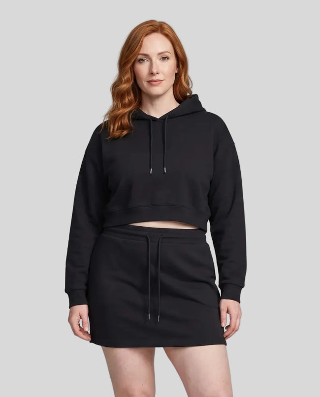 A woman modeling a matching black two-piece loungewear set consisting of Everyday Cropped Hoodie and Everyday Drawstring Skirt, paired with white sneakers.