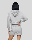 A model from behind wearing a Flower Gray Everyday Cropped Hoodie and matching Everyday Drawstring mini skirt set, paired with white sneakers.