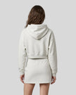 A model from behind wearing an Oat Gray Everyday Cropped Hoodie and matching Everyday Drawstring mini skirt set, paired with white sneakers.