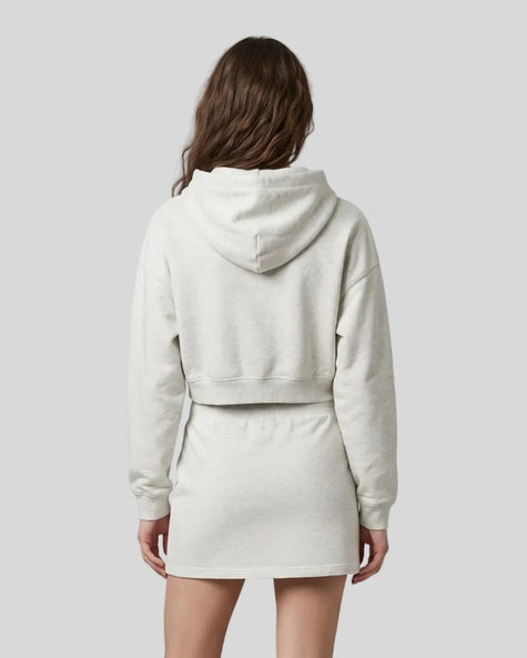 A model from behind wearing an Oat Gray Everyday Cropped Hoodie and matching Everyday Drawstring mini skirt set, paired with white sneakers.