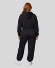 A model viewed from the back wearing a matching black Everyday Cropped Hoodie and Everyday Jogger Pants set, paired with white sneakers.