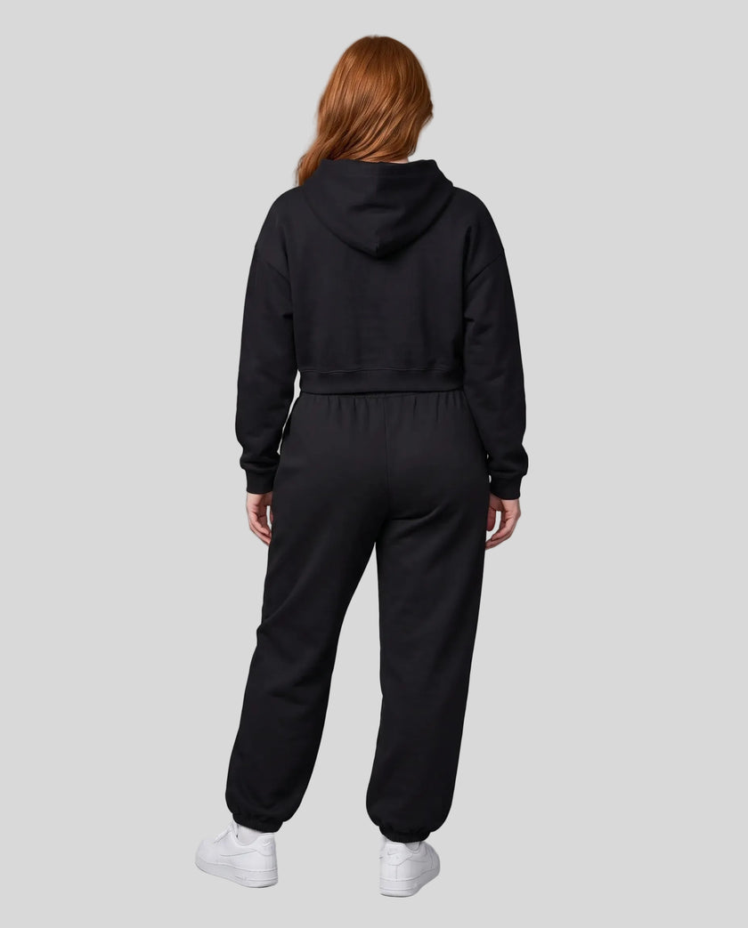A model viewed from the back wearing a matching black Everyday Cropped Hoodie and Everyday Jogger Pants set, paired with white sneakers.