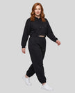 A woman modeling a black Everyday Cropped Hoodie and matching Everyday Jogger Pants set with white sneakers.