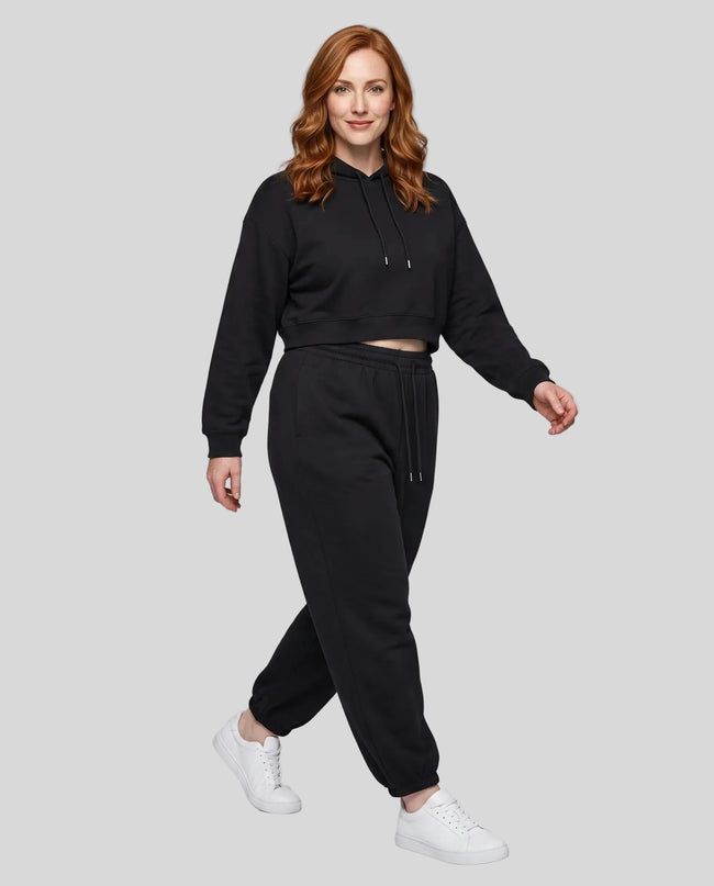 A woman modeling a black Everyday Cropped Hoodie and matching Everyday Jogger Pants set with white sneakers.