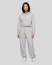 A woman modeling a flower gray Everyday Cropped Hoodie and matching Everyday Jogger Pants set with white sneakers.