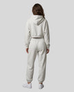 A model viewed from the back wearing a matching oat gray Everyday Cropped Hoodie and Everyday Jogger Pants set, paired with white sneakers.