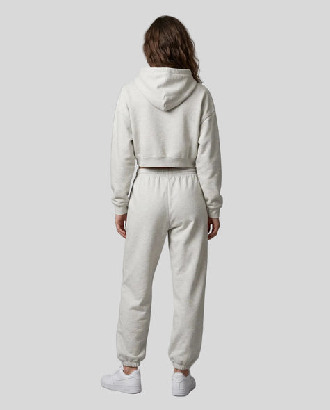 A model viewed from the back wearing a matching oat gray Everyday Cropped Hoodie and Everyday Jogger Pants set, paired with white sneakers.