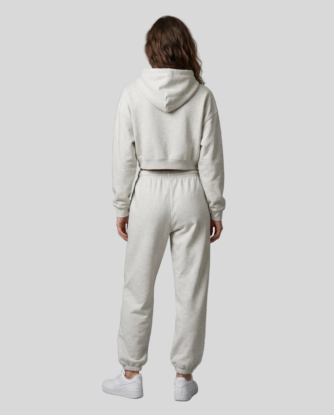 A model viewed from the back wearing a matching oat gray Everyday Cropped Hoodie and Everyday Jogger Pants set, paired with white sneakers.