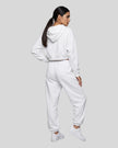 A model viewed from the back wearing a matching white Everyday Cropped Hoodie and Everyday Jogger Pants set, paired with white sneakers.