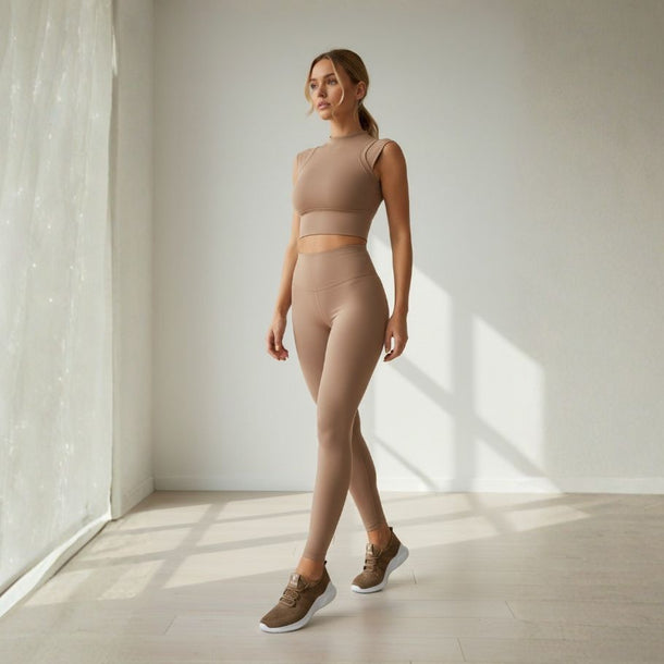 Woman wearing Athlesi activewear set in beige neutral tones athletic wear standing in a well-lit room with wooden floor and white walls, highlighting fit, stretch, and everyday comfort.